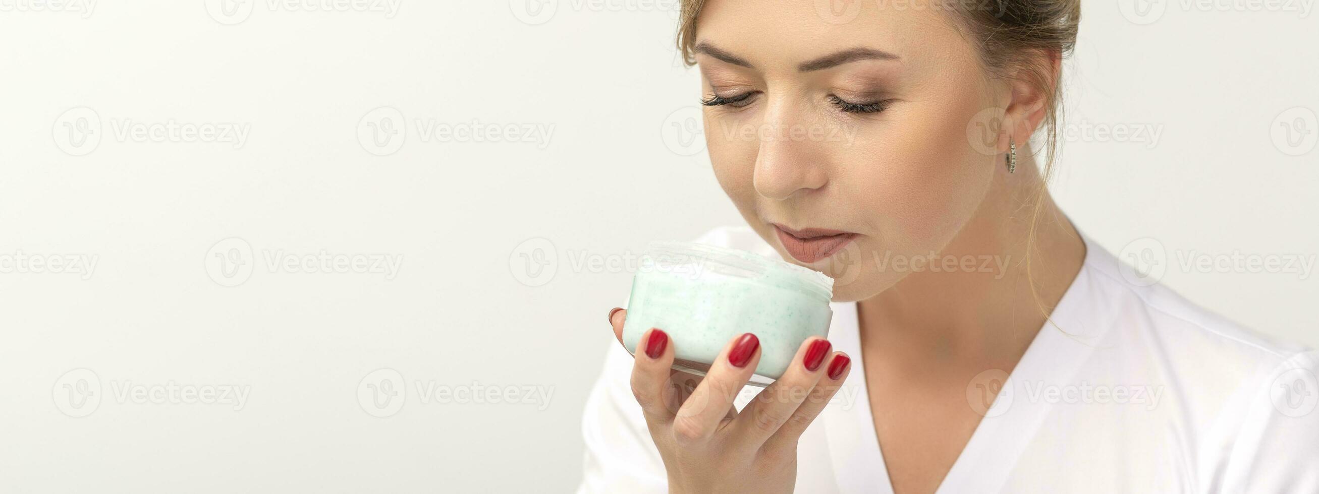 retrato de joven cosmetólogo olfateando hidratante crema participación blanco tarro en blanco fondo, Copiar espacio. foto