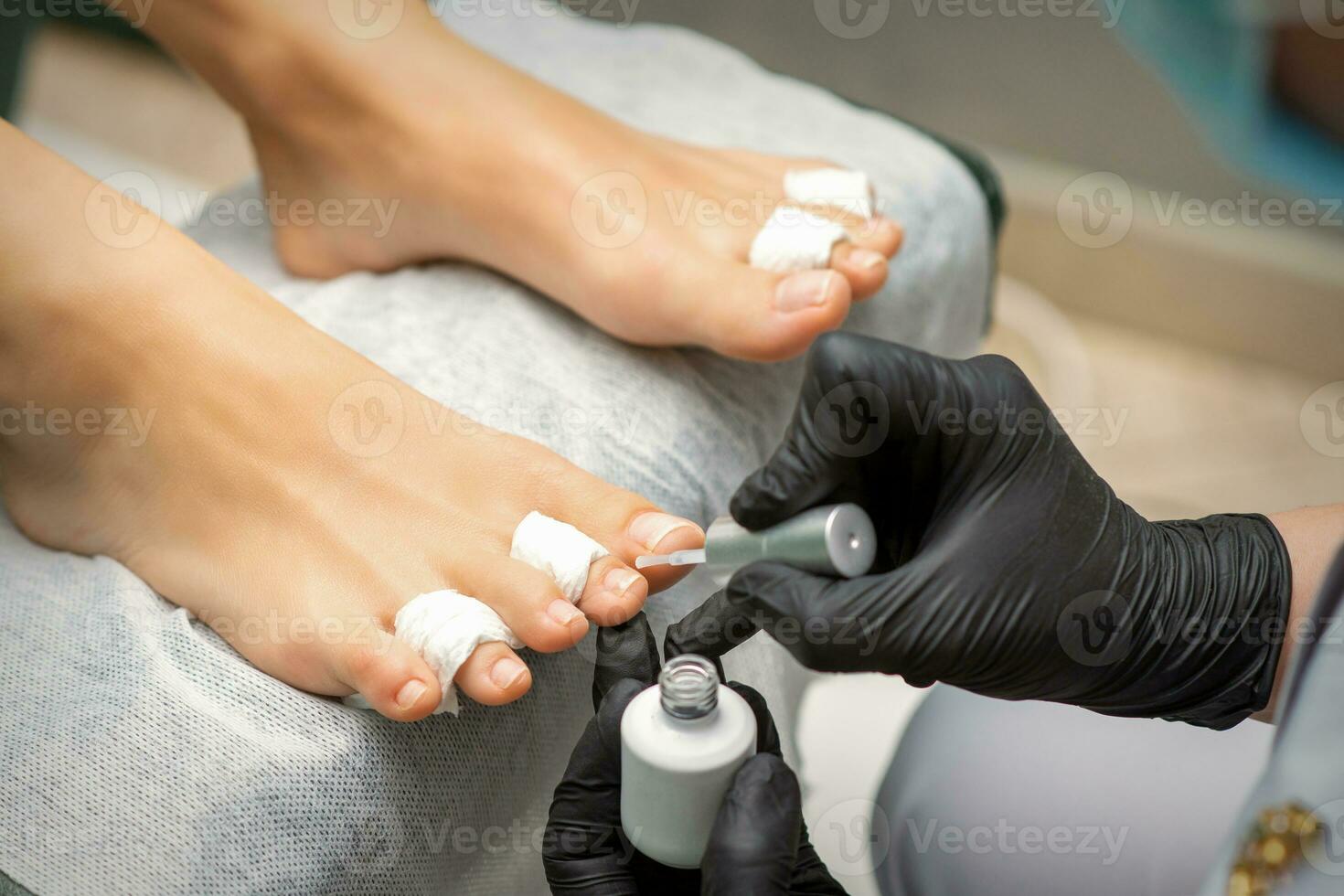 pedicuro aplicando transparente barniz a el hembra uñas de los pies en un belleza salón. foto