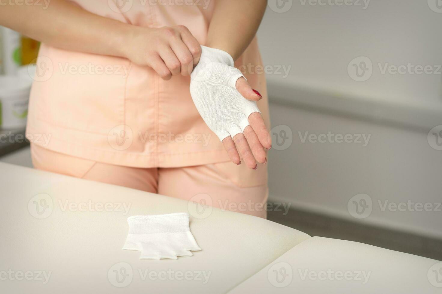 Cosmetologist in workwear wearing white bamboo fingerless gloves on her hands. photo