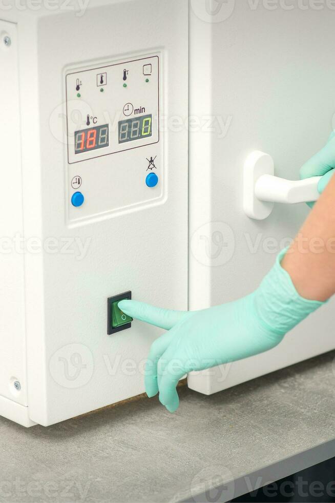 Beautician in protective gloves starts the machine for disinfection of tools before the depilation procedure. photo