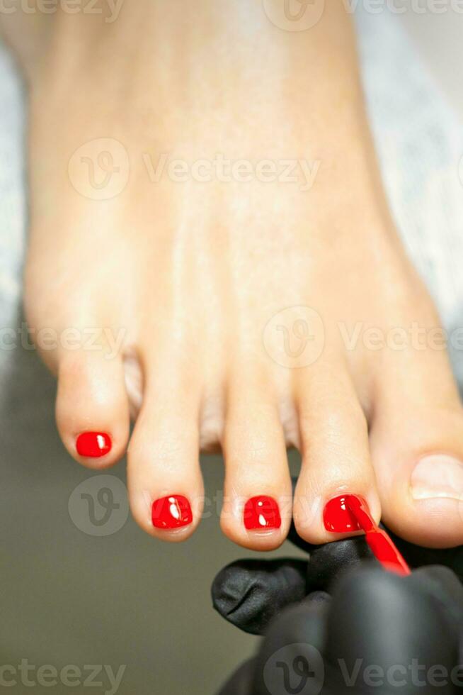 pedicuro aplicando rojo uña polaco a el hembra uñas de los pies en un belleza salón. foto