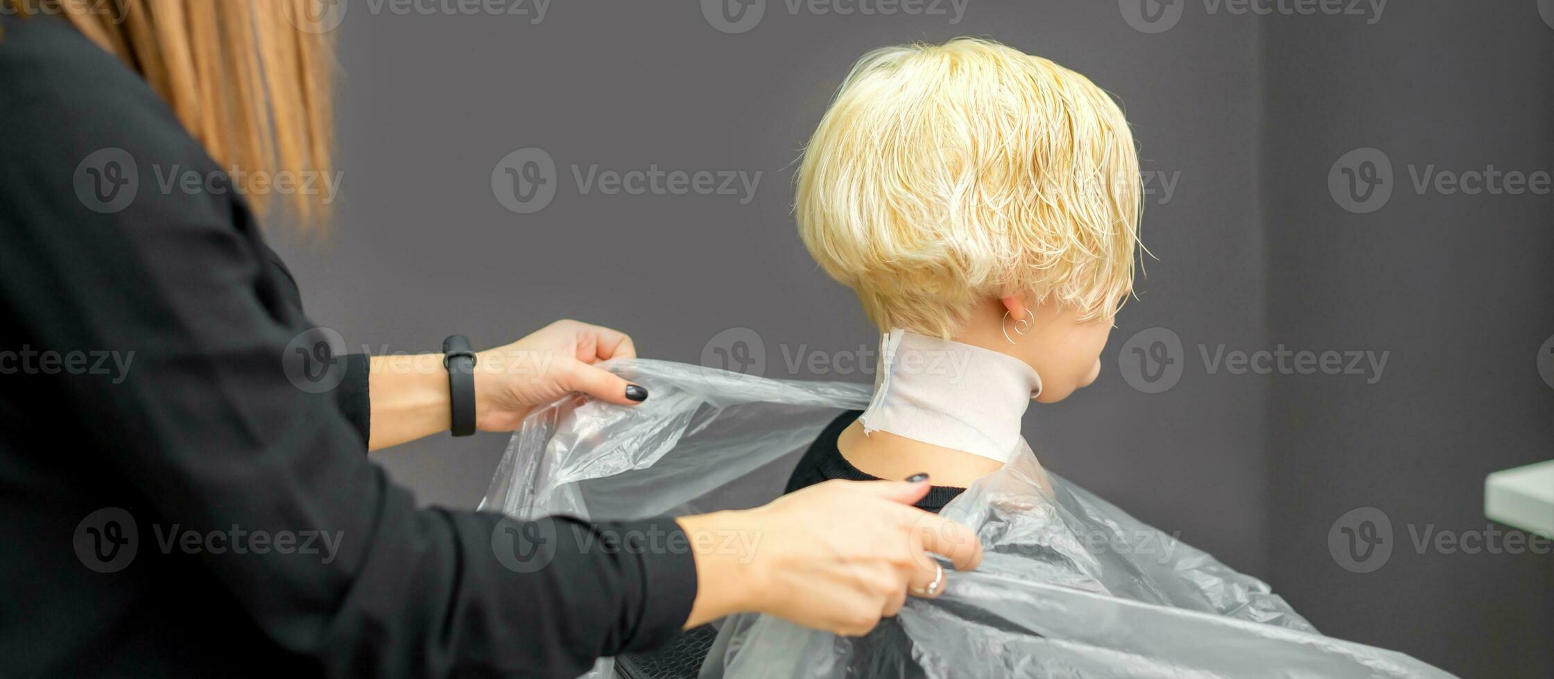 Hairstylist covers neck with cape for a female client in a beauty salon. photo