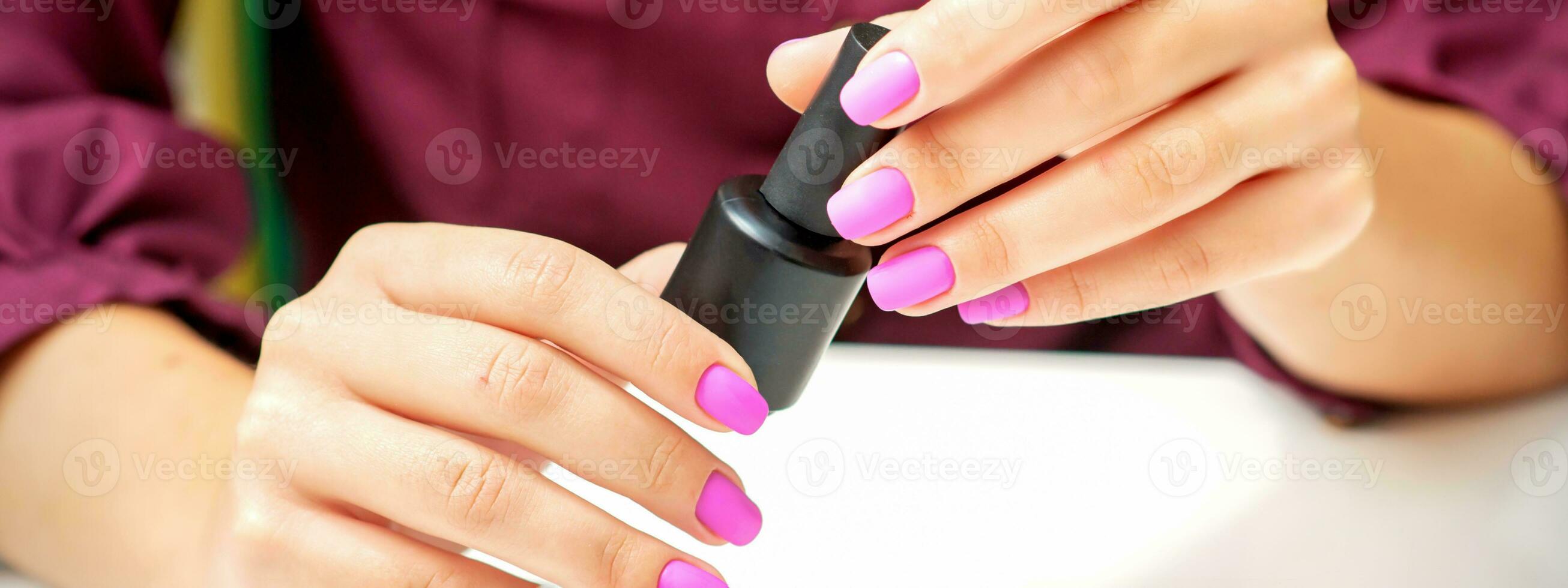 White woman holding nail polish black bottle with painted pink nails close up. photo