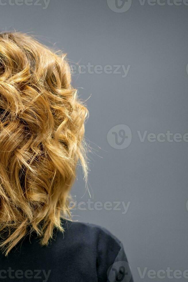 Back view of the woman with long brown curly hair stands on a dark background. photo