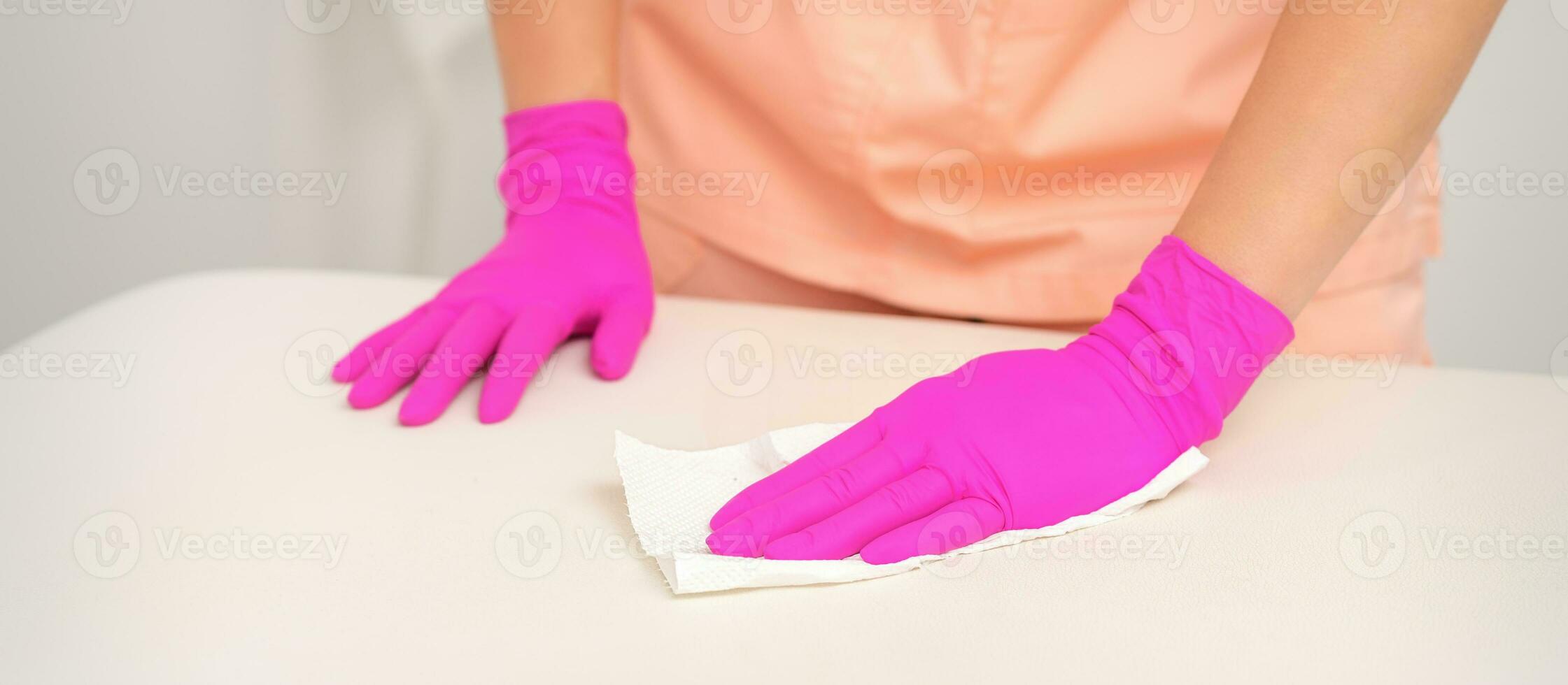 Close up of hands in rubber protective pink gloves cleaning the white surface with a white rag. photo