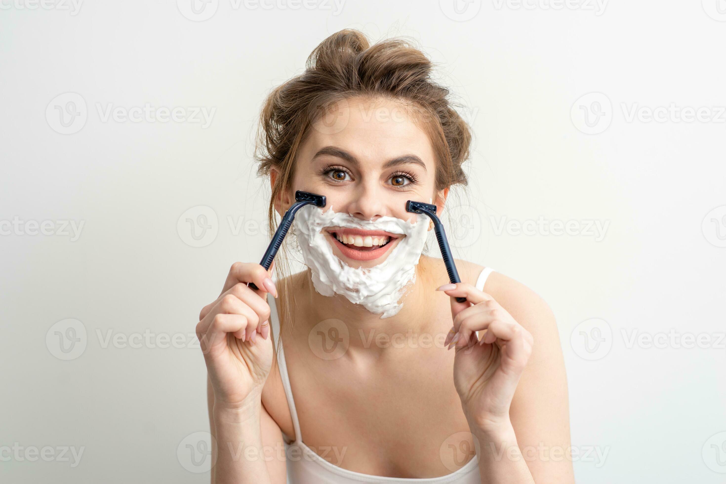 Beautiful young caucasian woman shaving her face by razor on white background. Pretty smiling