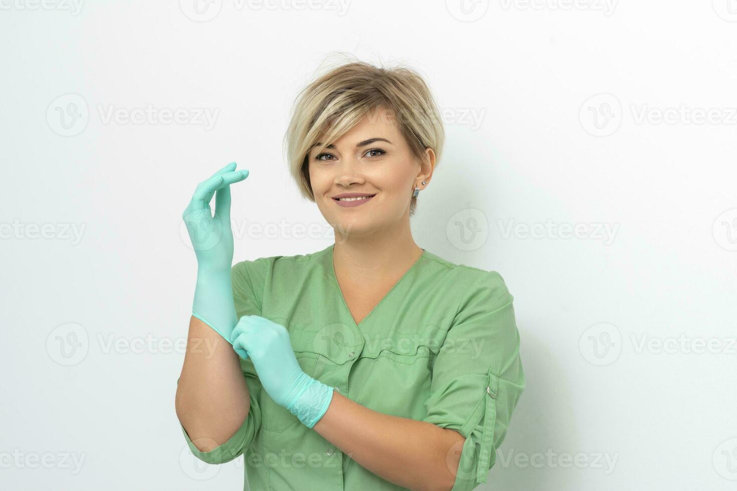 médico cosmetólogo pone en estéril azul guantes sonriente prepara a recibir clientela en blanco. foto