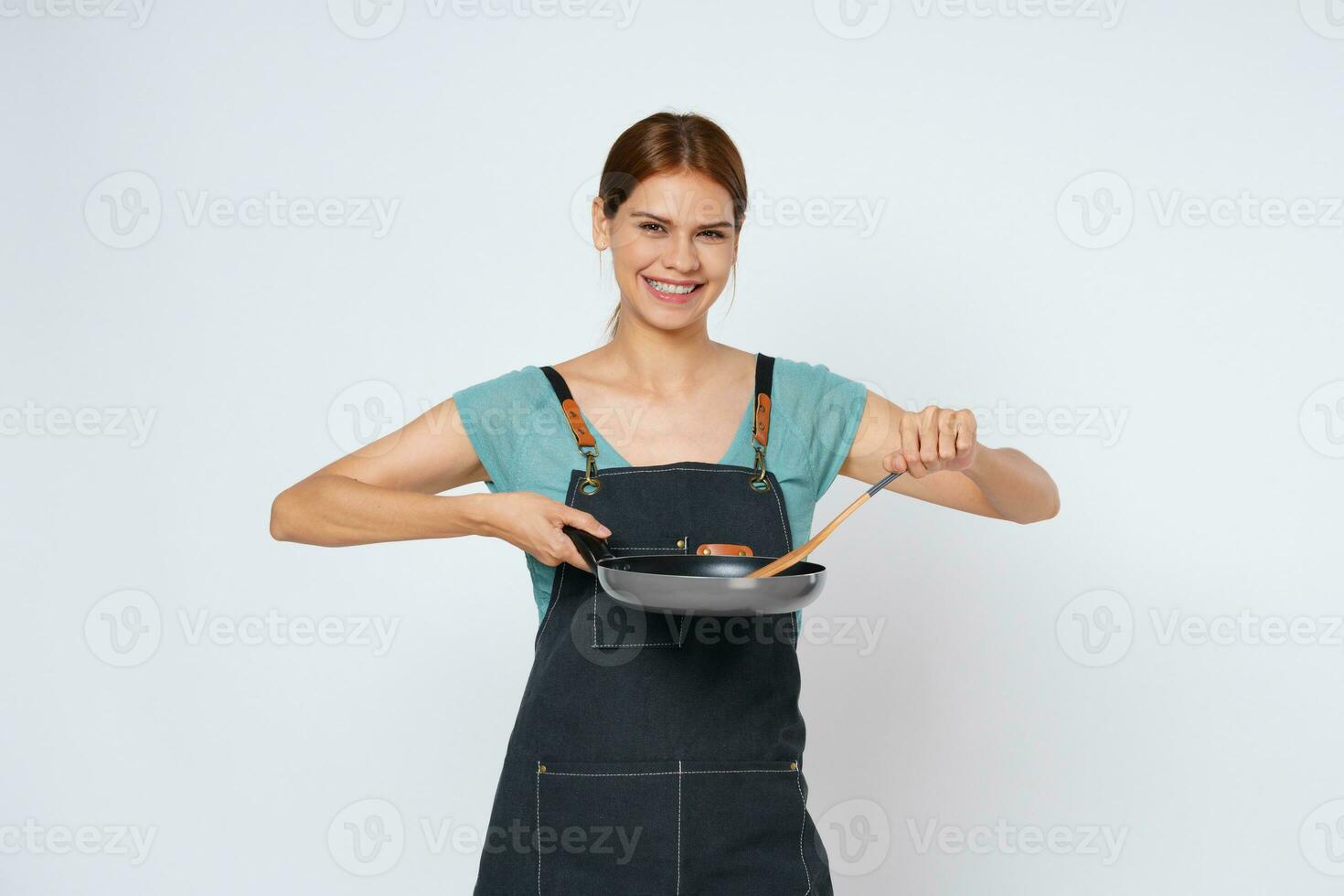 Young woman wearing kitchen apron cooking and holding pan and spatula isolated on white background. photo