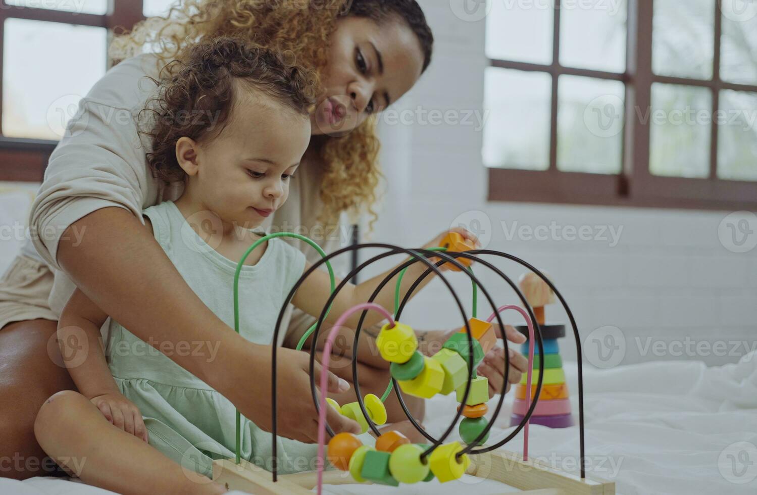 Happy mother and daughter playing with a toy developing colorful wooden blocks on bed together at home. photo