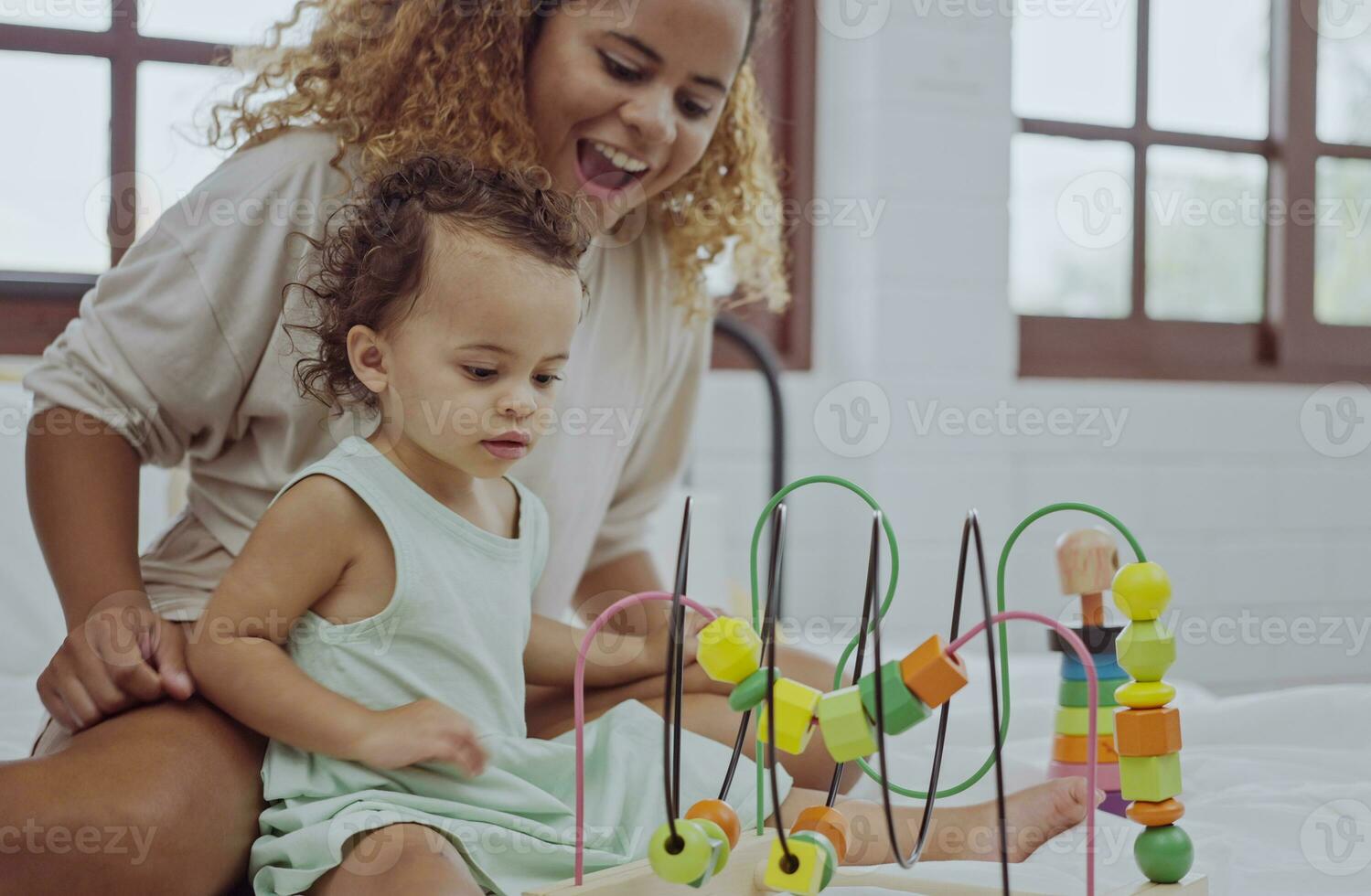 Happy mother and daughter playing with a toy developing colorful wooden blocks on bed together at home. photo