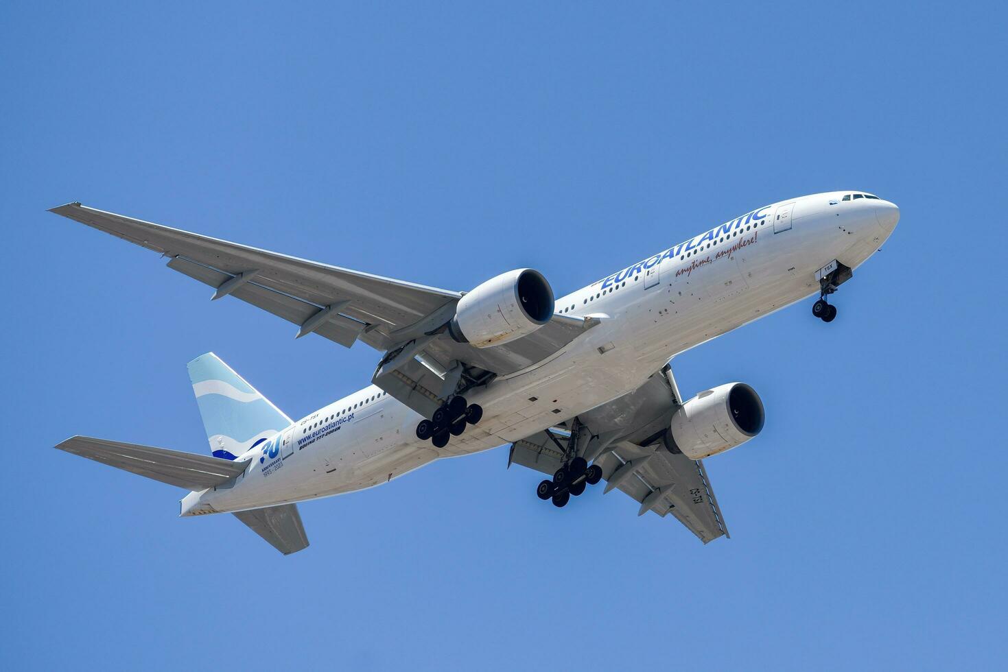 Portuguese air company Euroatlantic with aircraft Boeing 777-200ER approaching to land at Lisbon International Airport against blue sky photo