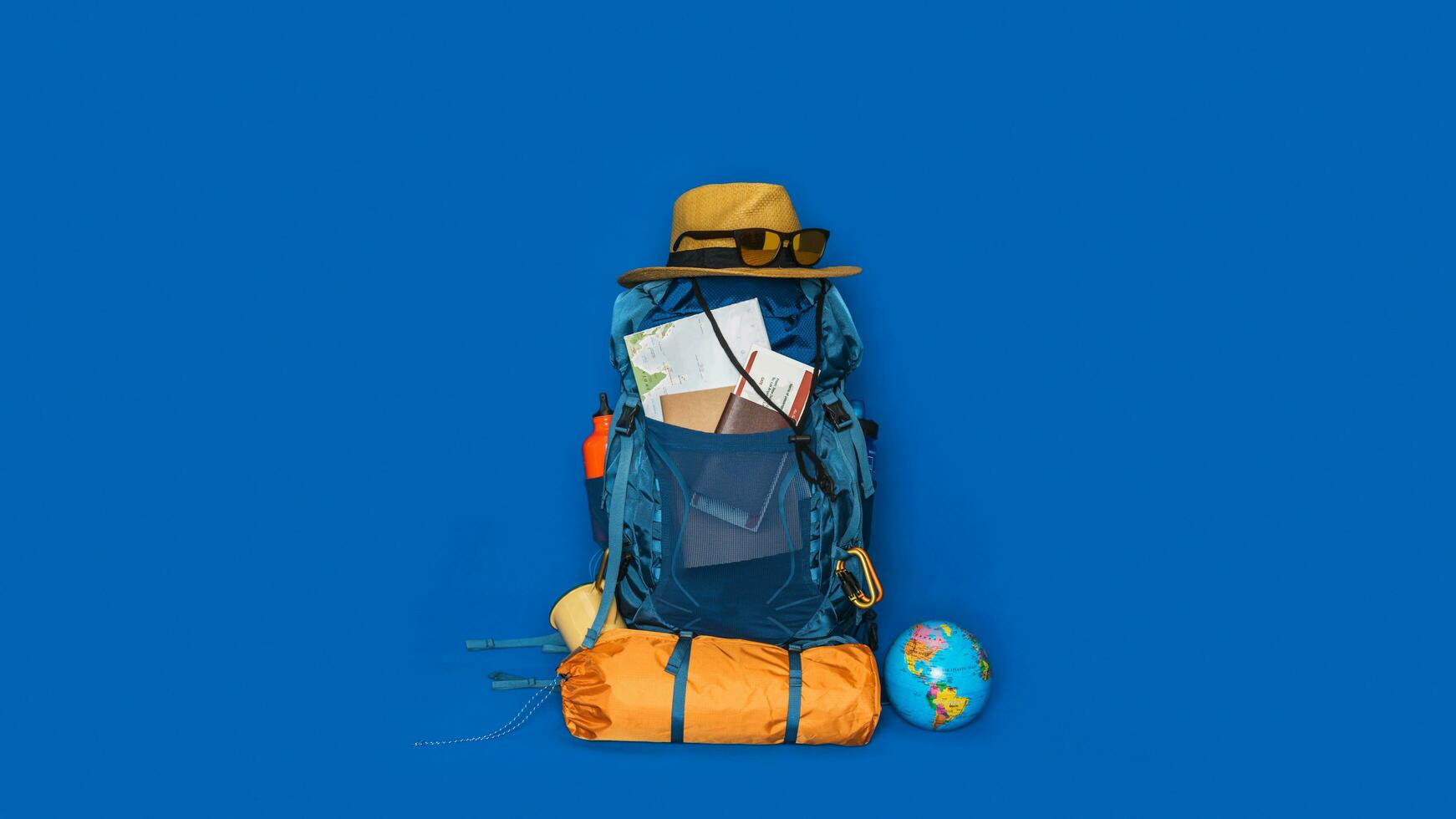 vacaciones de planificación turística con la ayuda del mapa del mundo con otros accesorios de viaje alrededor. concepto de equipaje con accesorio para las vacaciones de los viajeros sobre fondo de color azul. mochila de viaje foto