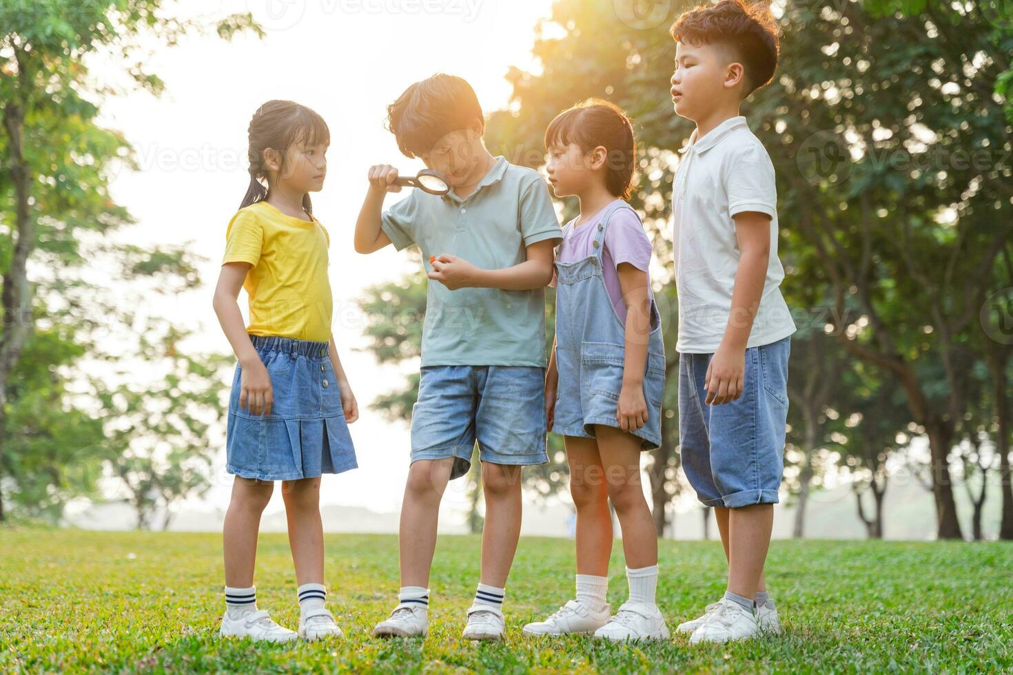 image of asian kids using magnifying glass in park photo