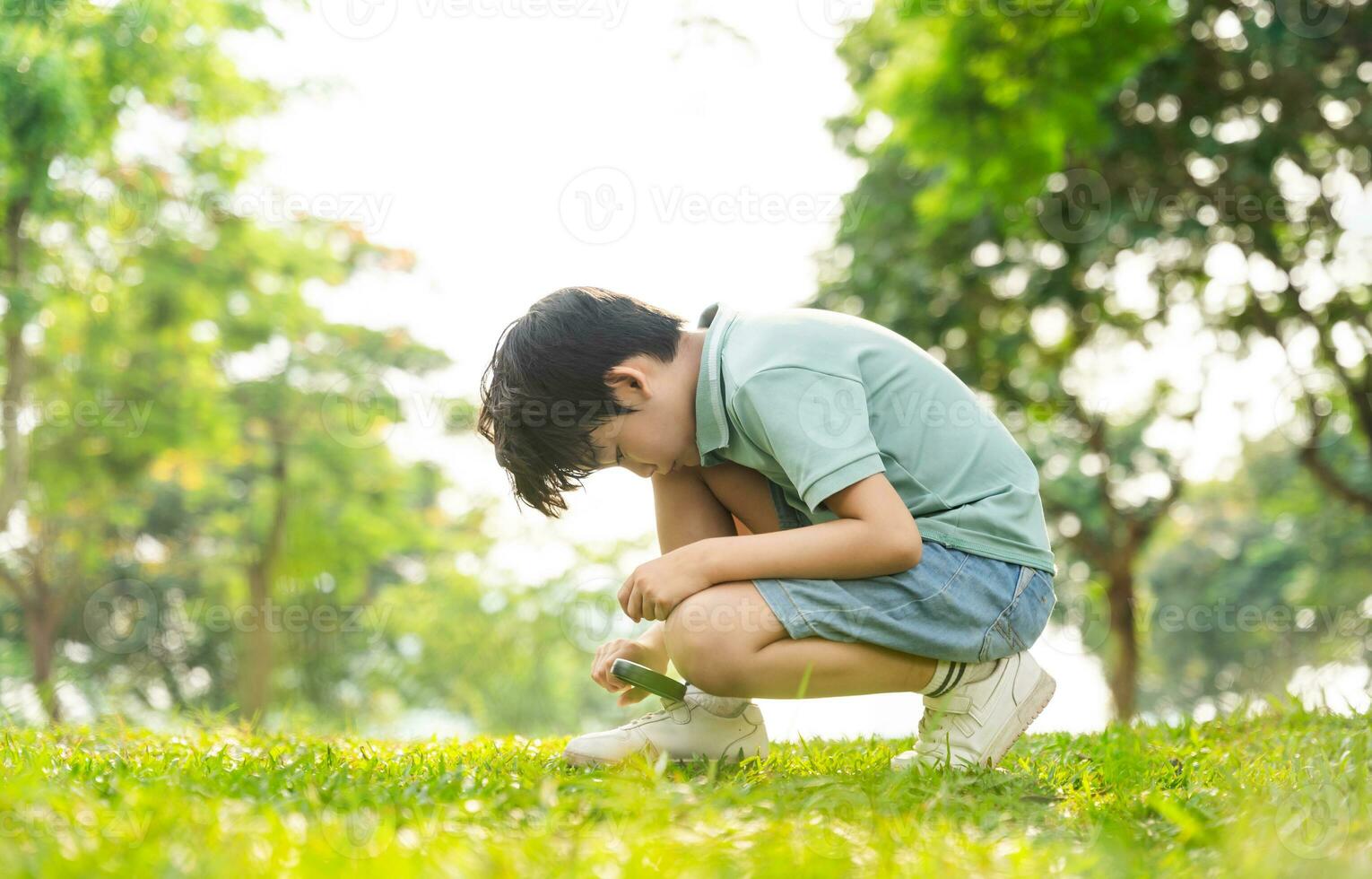 image of asian boy using magnifying glass in park photo