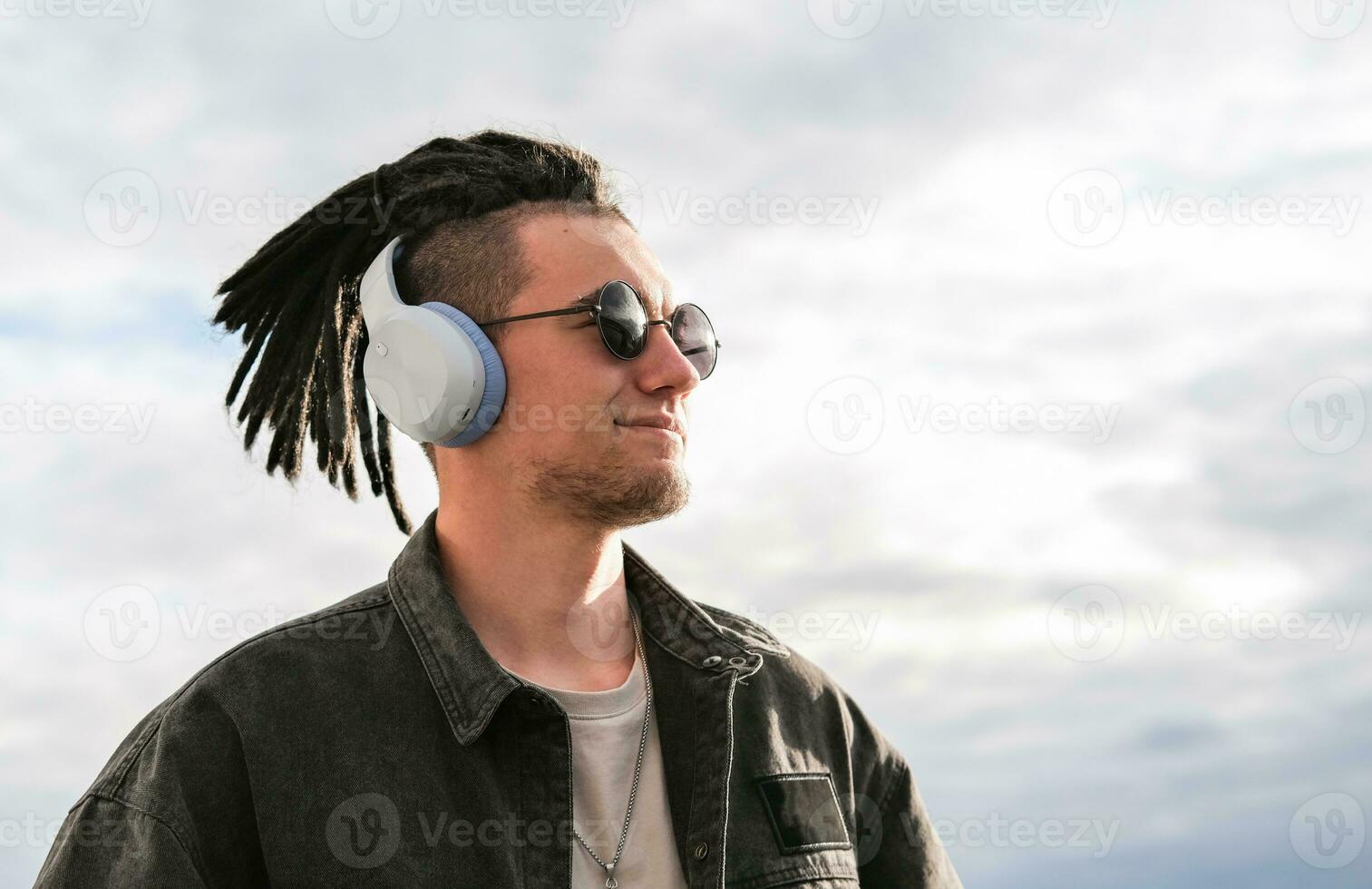 retrato de un joven chico con rastas y piercings escuchando a música en auriculares y disfrutando momento foto