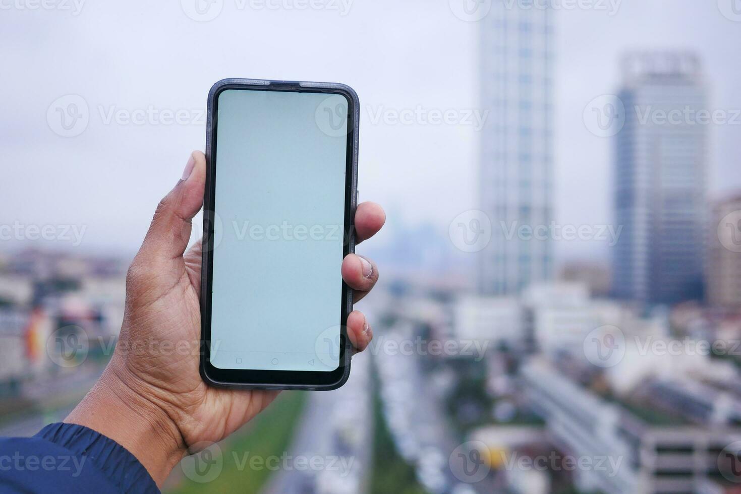 young man hand using smart phone with green screen against city buildings photo