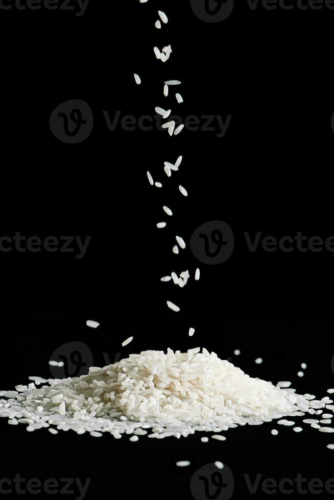 Raw white rice is falling on table. Pile of uncooked long rice on black background. photo