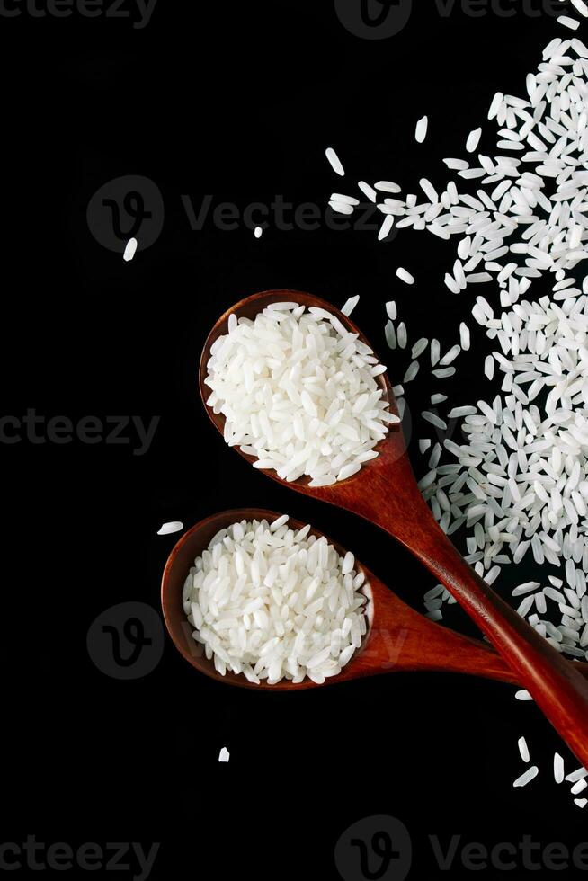 White long rice in wooden spoons on black background. Raw uncooked rice grains enriched with vitamins. photo