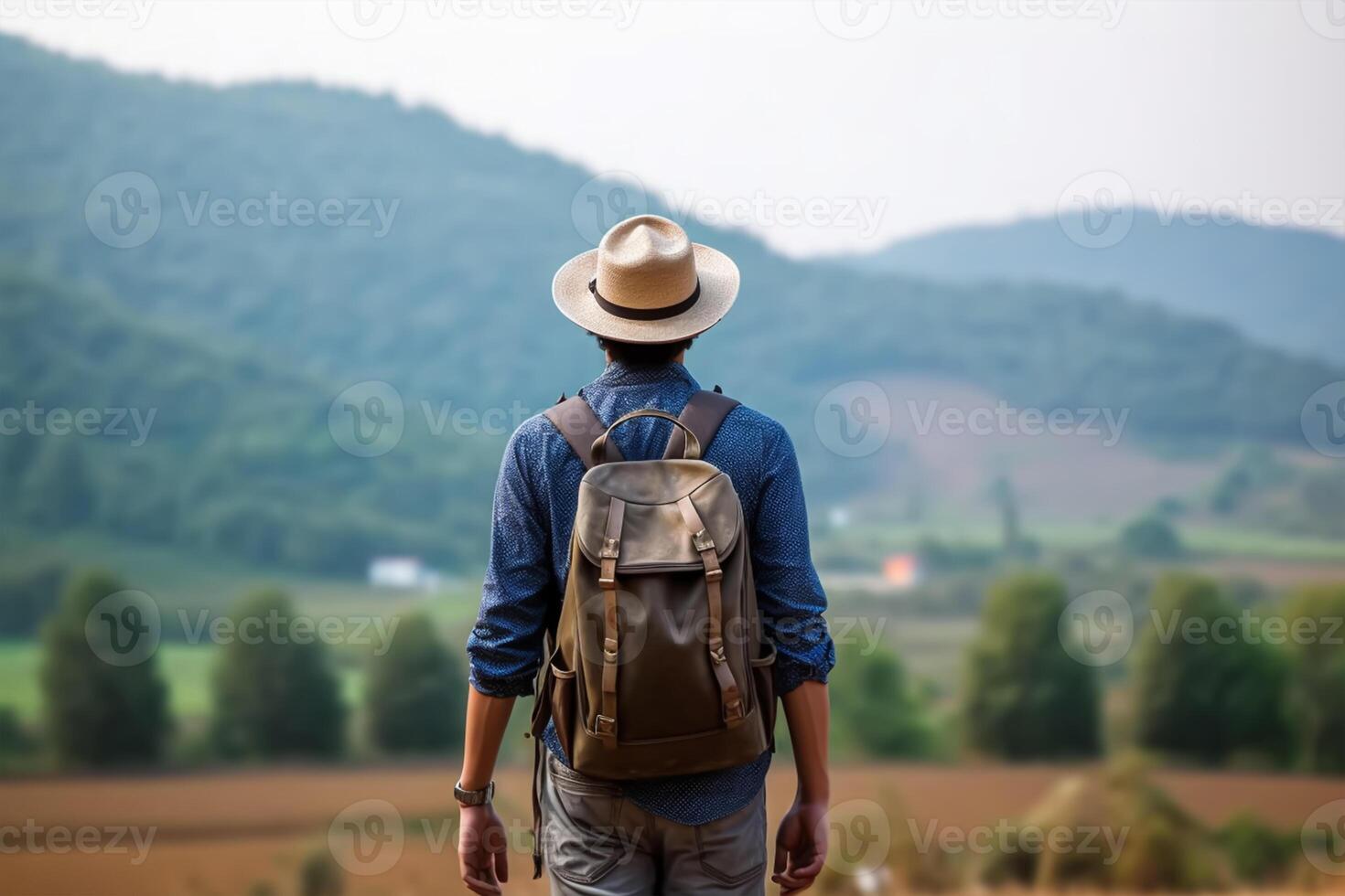 Back view of young man with backpack and hat standing on top of the mountain photo