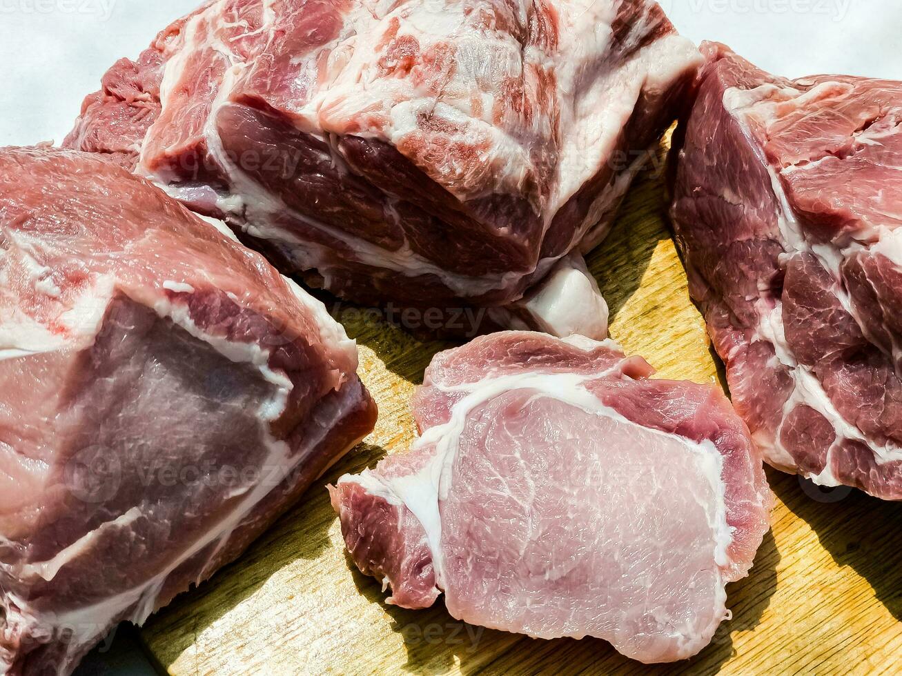 Fresh cuts of various parts of a pig carcass on a wooden kitchen board. Pieces of pig meat close-up photo