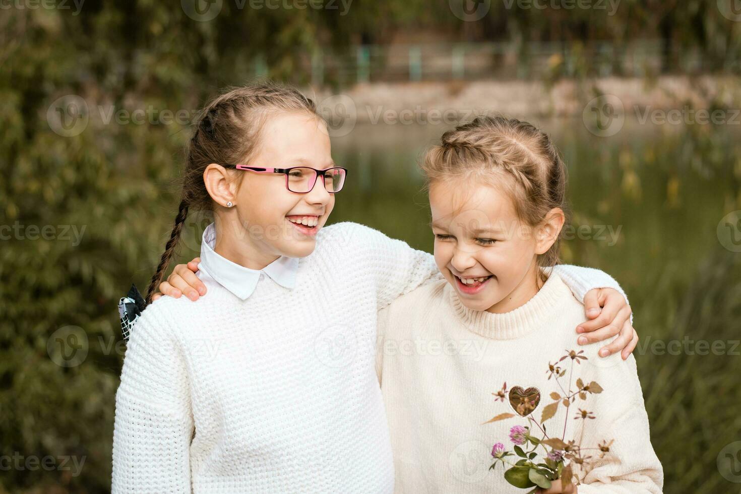 Two schoolgirls walk, hug and laugh after school in the park. Back to school concept photo