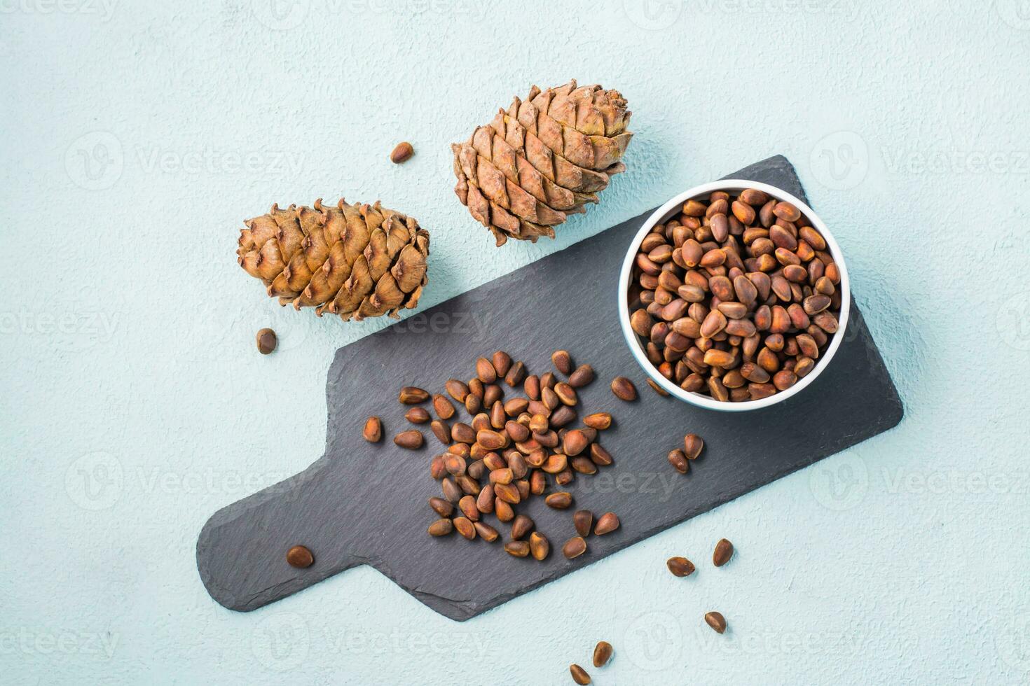 Unpeeled pine nuts and cones on a slate board and in a bowl. Gifts of Siberia. Detox and cure for insomnia. Healthy vitamin nutrition. Top view photo