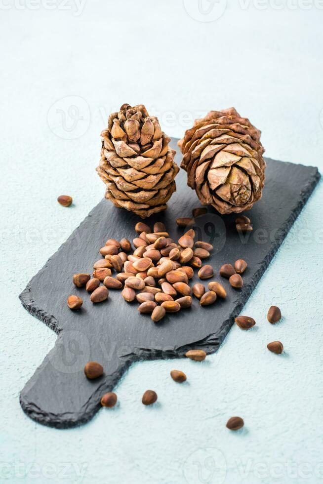 Unshelled pine nuts and cones on a slate board. Gifts of Siberia. Detox and cure for insomnia. Healthy vitamin nutrition. Vertical view photo