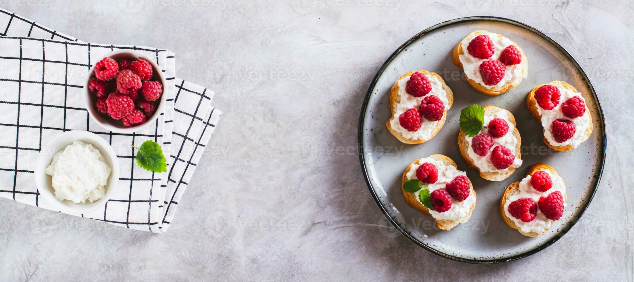 Sweet bruschettas with curd cheese and raspberries on a plate top view web banner photo