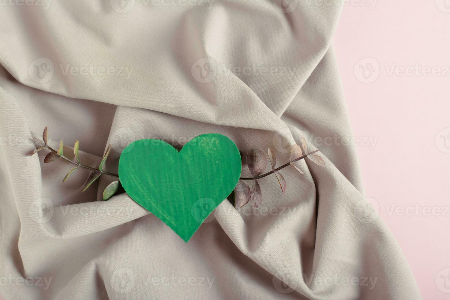 Green cardboard heart and eucalyptus branches on a background of green crumpled cotton fabric photo