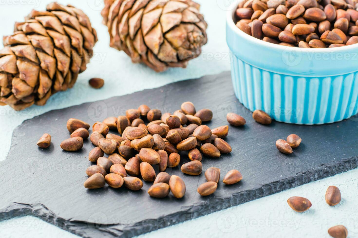 A handful of unpeeled pine nuts on a slate board, pine cones and nuts in a bowl. Detox and cure for insomnia. Healthy vitamin nutrition photo