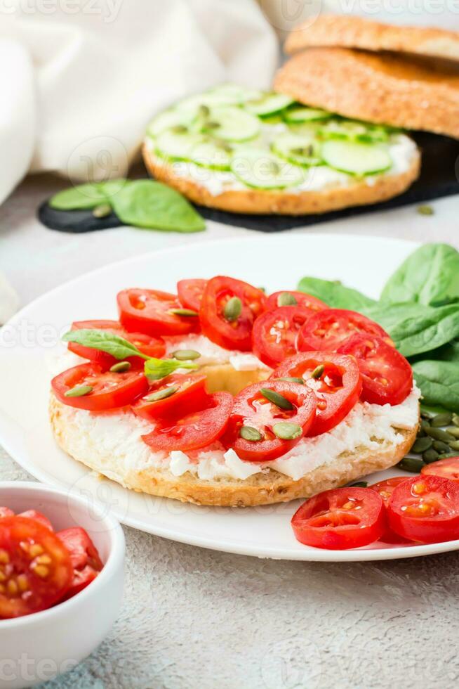 Delicious bagel stuffed with feta, tomatoes and pumpkin seeds and spinach leaves on a plate. Light Healthy Vitamin Snack. Vertical view. Close-up photo