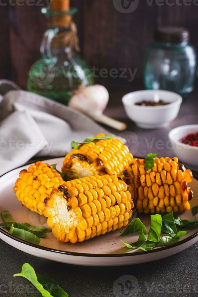 Baked sweet corn cobs with butter, garlic and herbs on a plate vertical view photo