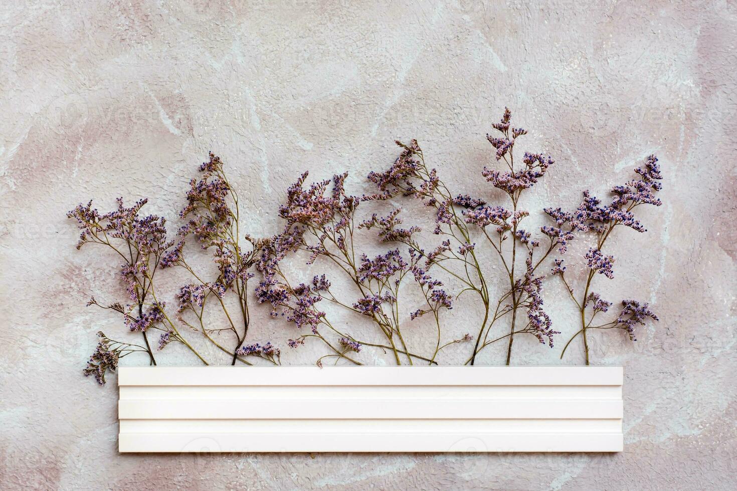 Dry purple flowers behind a white wooden border on a textured background. Romantic greeting vintage card. Top view photo