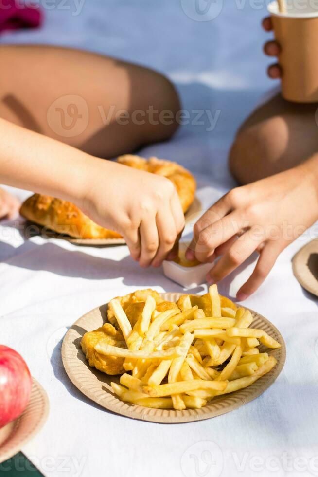 Two schoolgirls eat fries at a picnic in the park. Eco-friendly disposable tableware. School meals. Vertical view photo