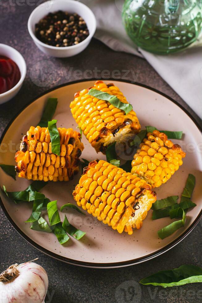 Grilled corn with spices, butter and garlic on a plate on the table vertical view photo