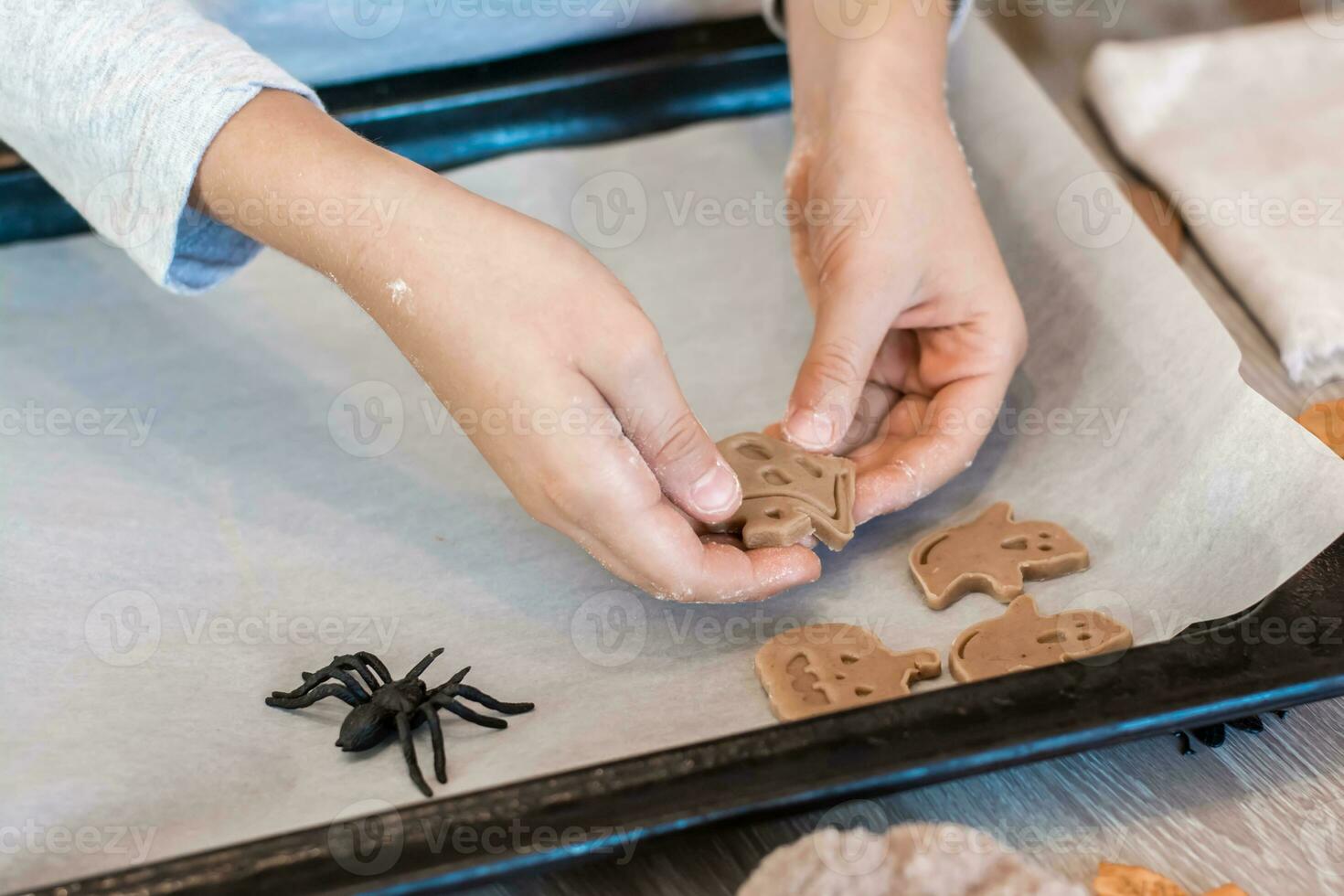 Preparing to celebrate halloween and preparing a treat. Children's hands lay raw halloween cookies on a baking sheet. Lifestyle photo
