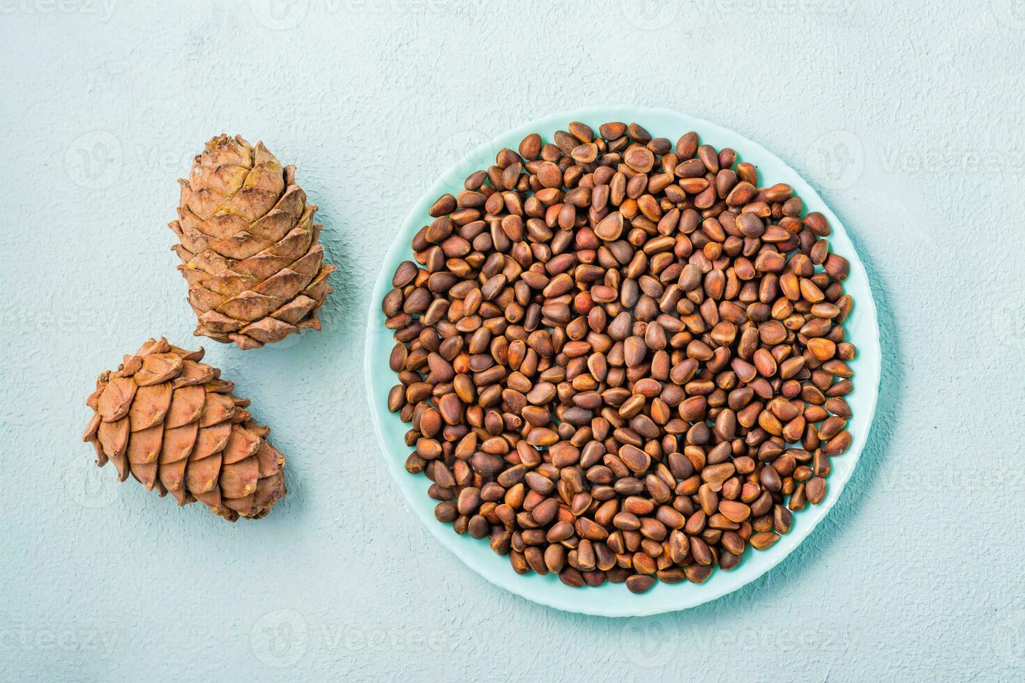 Unpeeled pine nuts on a blue plate and cones. Remedy for insomnia and detox food. Vitamins and health. Top view photo