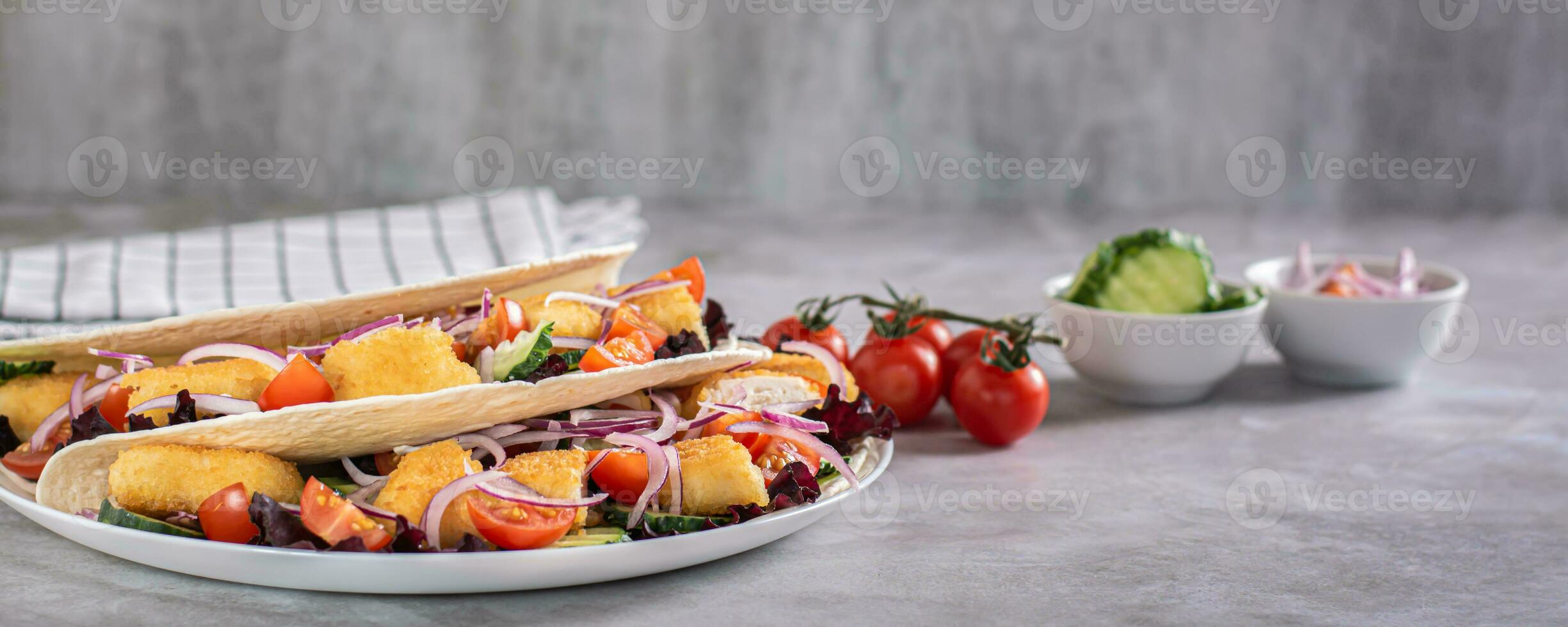Delicious tortilla with chicken nuggets, vegetables, onions and lettuce on a plate web banner photo