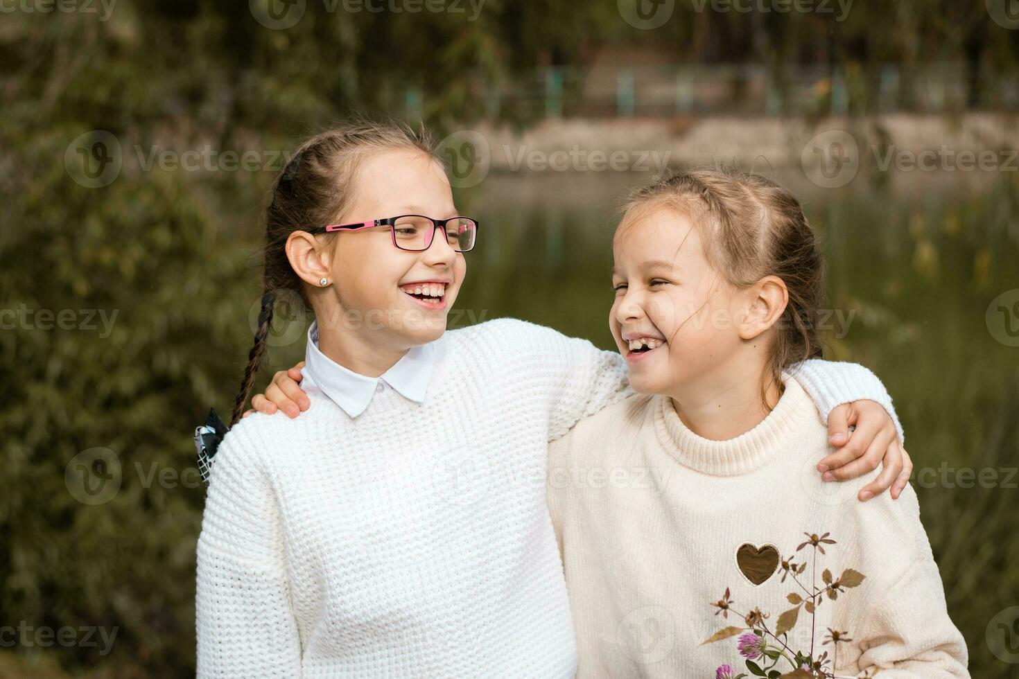 Two schoolgirl sisters hug and laugh after school in the park. Back to school concept. Authentic style life photo