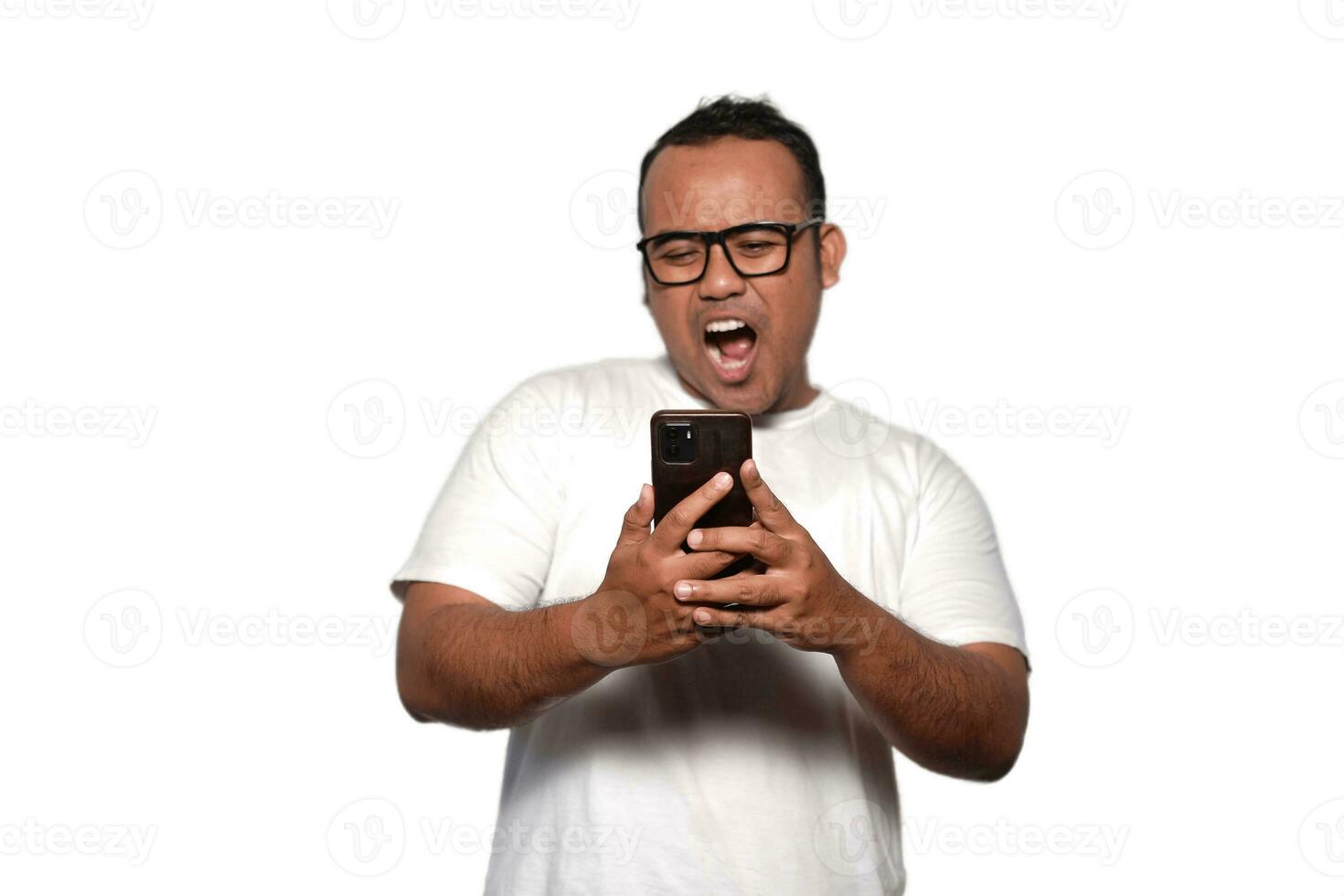 Excited Asian man with glasses wearing white Tshirt smiling while holding his phone, isolated by white background photo