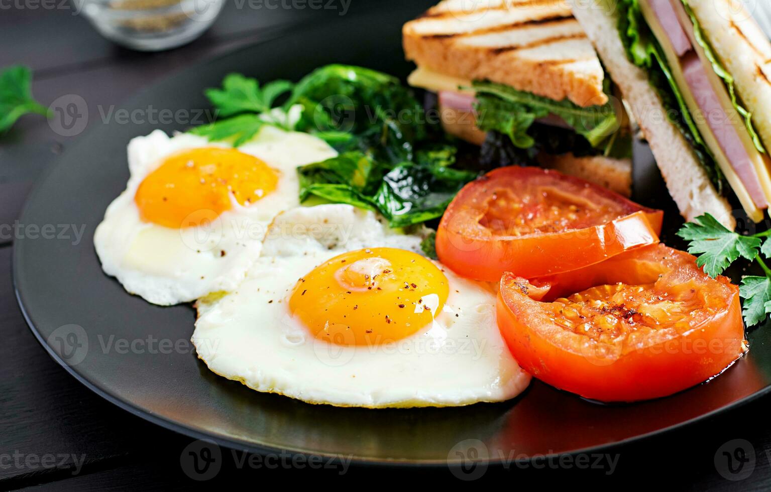 Breakfast. fried egg, spinach, tomatoes and club sandwich on plate. photo