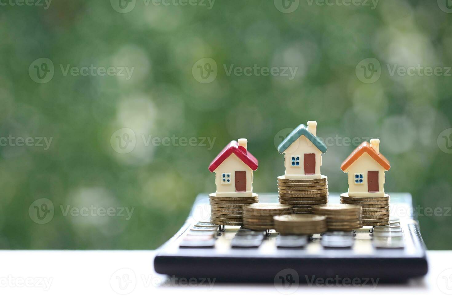 Finance, Model house on calculator and stack of coins money on natural green background,Business investment and real estate concept photo
