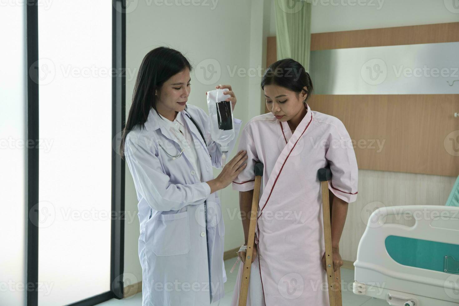 Asian female orthopedic doctor helping patient woman with saline to walk with crutches in a hospital clinic after physical therapy by muscle medical treatment recovery from injury. photo