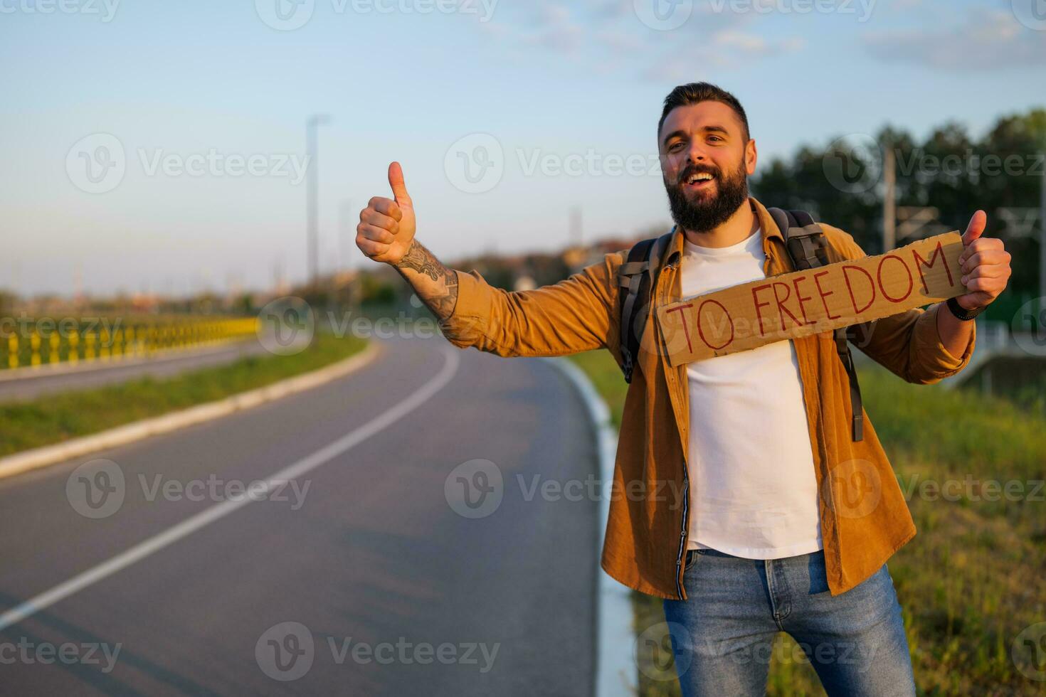 Man is hitchhiking on roadside trying to stop car. He is holding cardboard with inscription. photo