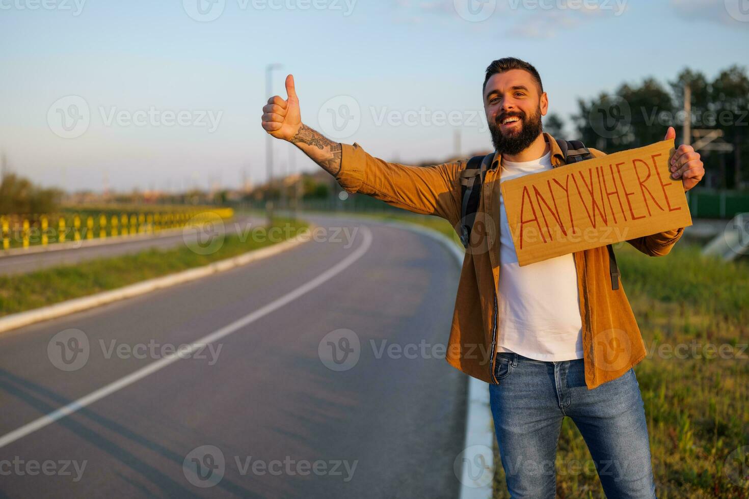 Man is hitchhiking on roadside trying to stop car. He is holding cardboard with inscription. photo