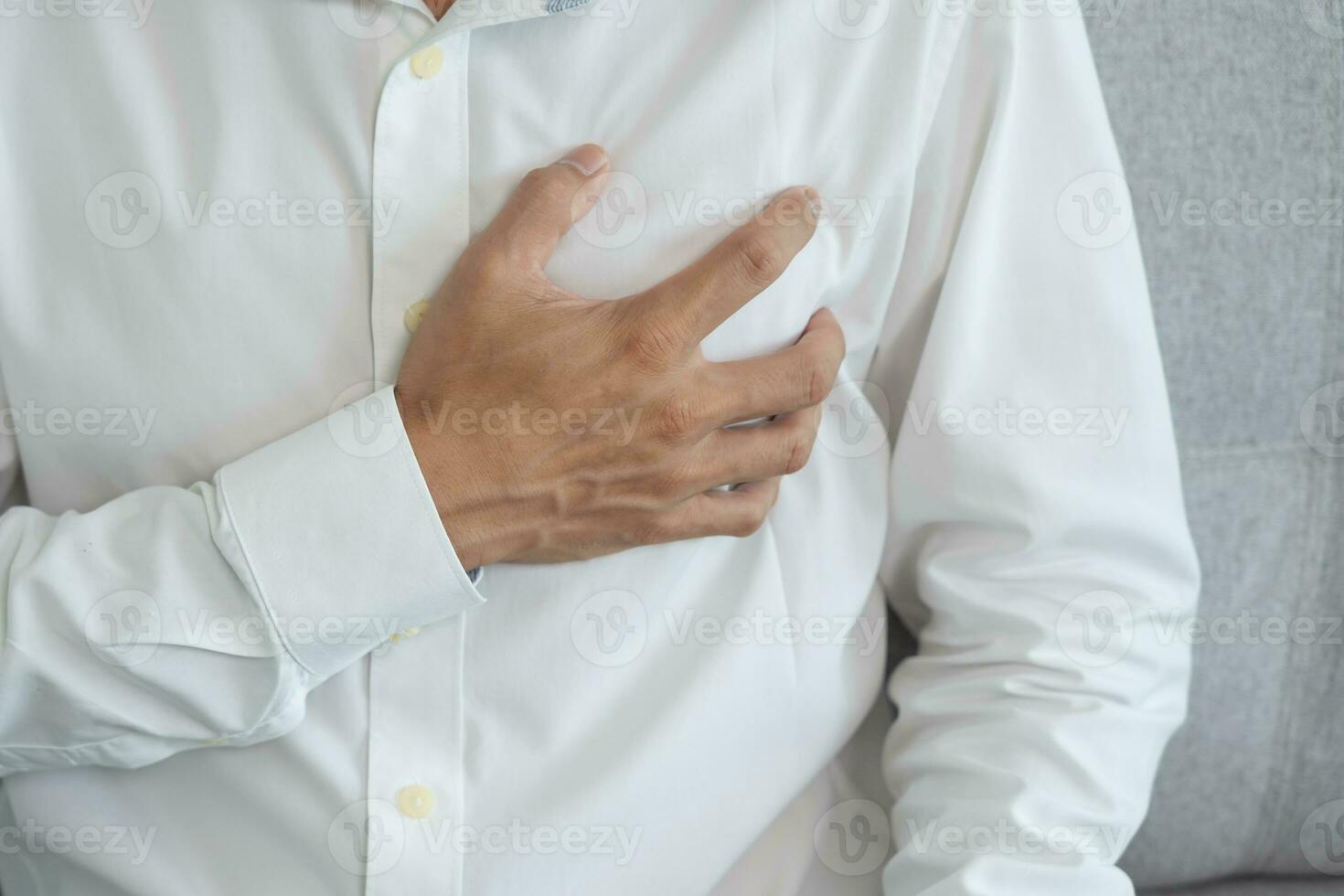 hand hold chest with heart attack symptoms, asian man working hard have chest pain caused by heart disease, leak, dilatation, enlarged coronary heart, press on the chest with a painful expression photo