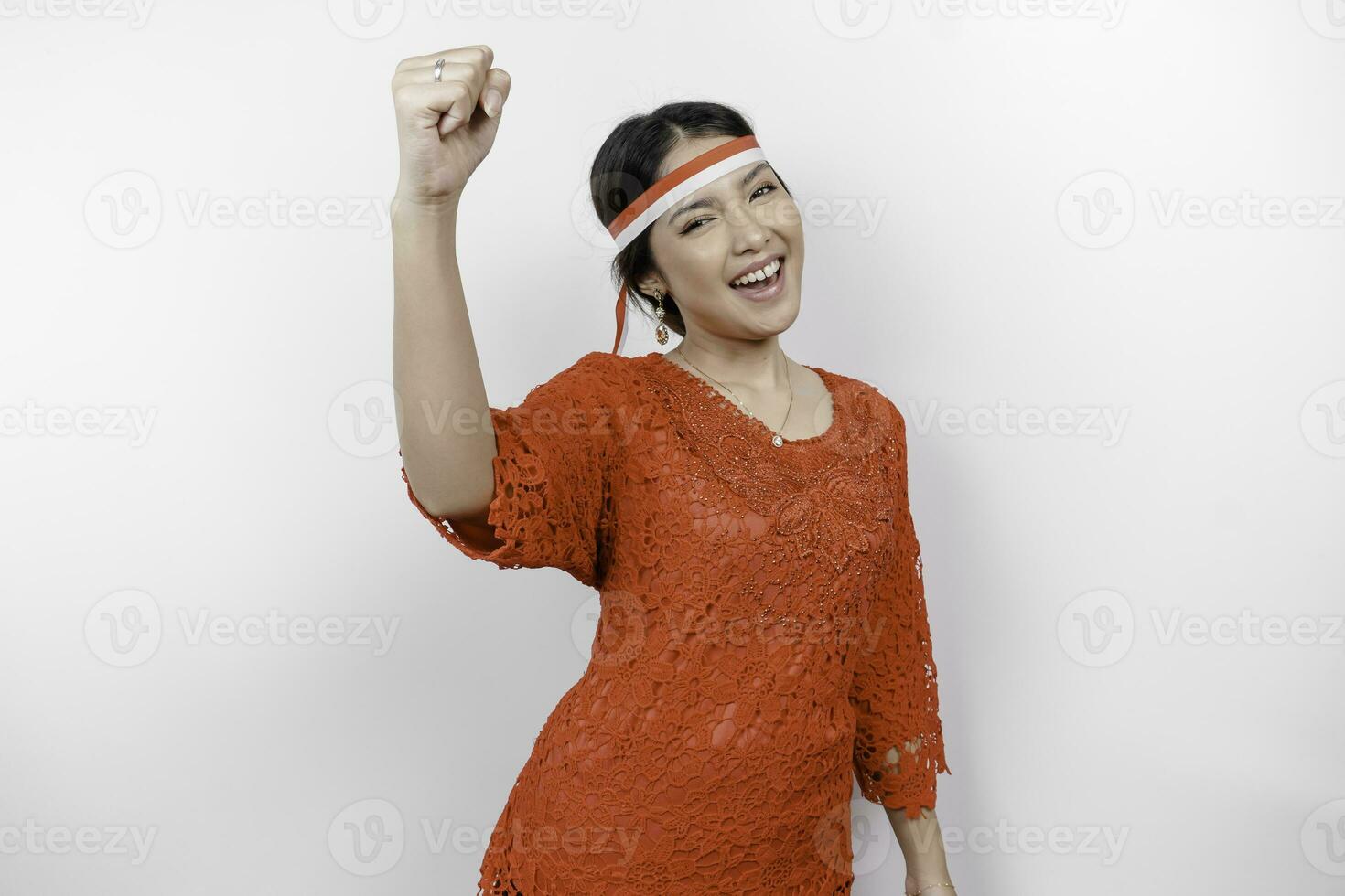 A young Asian woman with a happy successful expression wearing red kebaya and headband isolated by white background. Indonesia's independence day concept. photo