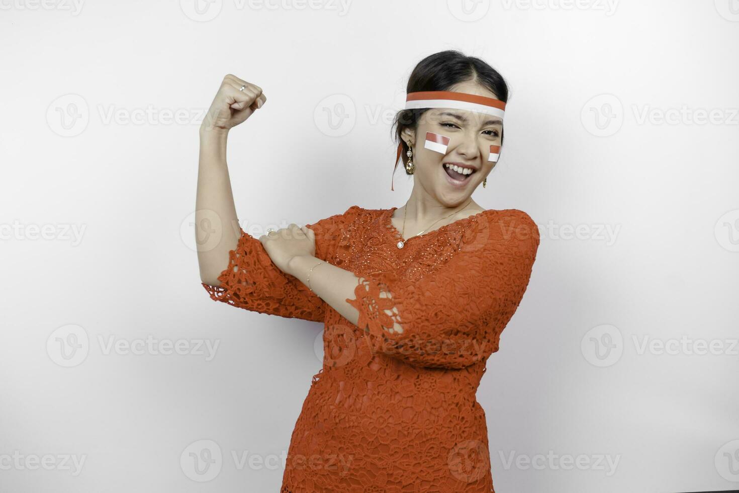 emocionado asiático mujer vistiendo un rojo kebaya y venda demostración fuerte gesto por levantamiento su brazos y músculos sonriente con orgullo de indonesia independencia día concepto. foto