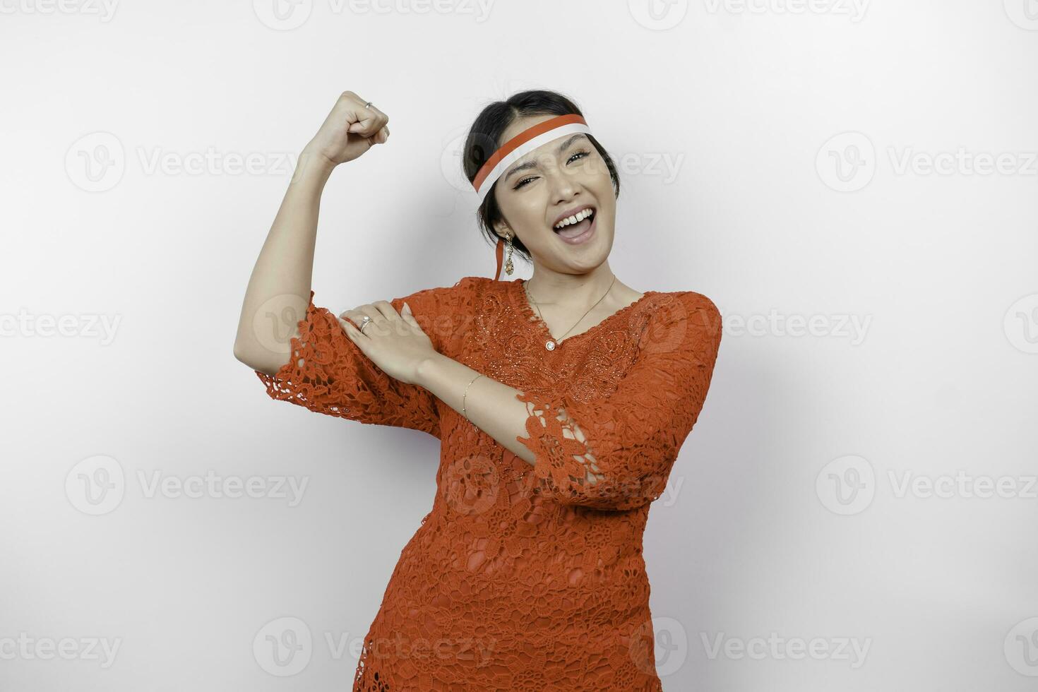 emocionado asiático mujer vistiendo un rojo kebaya y venda demostración fuerte gesto por levantamiento su brazos y músculos sonriente con orgullo de indonesia independencia día concepto. foto