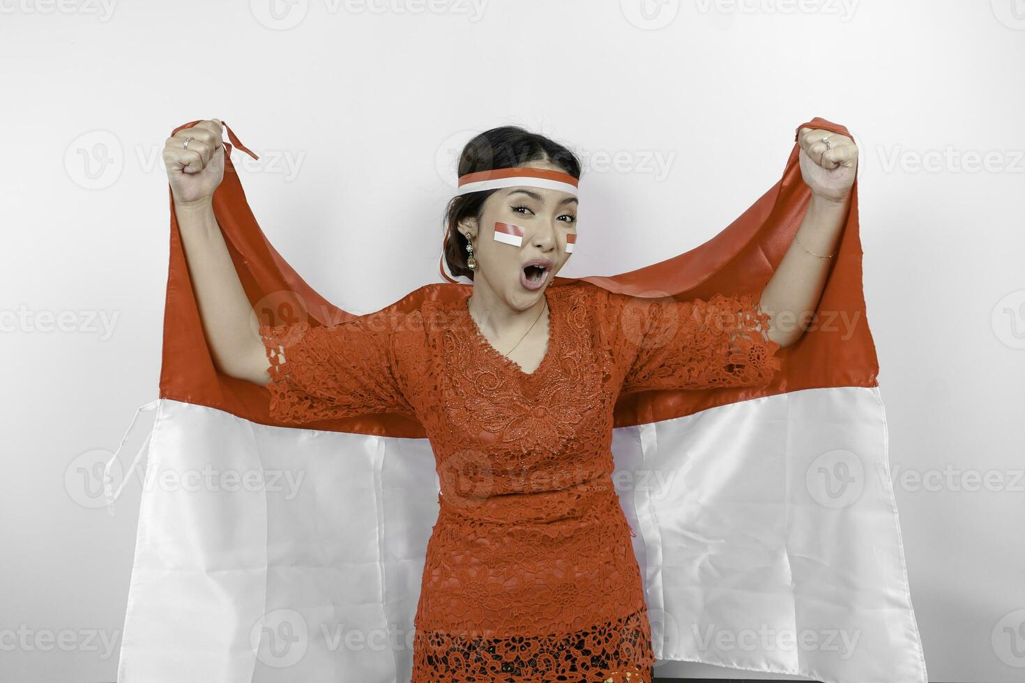 Happy smiling Indonesian woman wearing red kebaya and headband holding Indonesia's flag to celebrate Indonesia Independence Day isolated over white background. photo